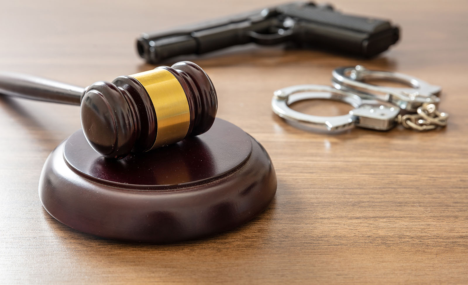 Judge gavel and handgun on lawyer office desk. Crime, murder punishment concept. Wooden courthouse table, close up view